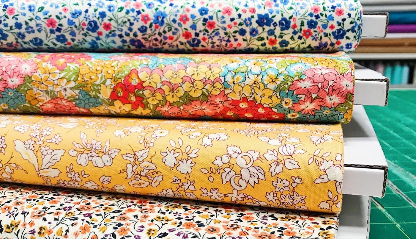 Floral fabric bolts stacked on a green cutting mat on the warehouse cutting table.