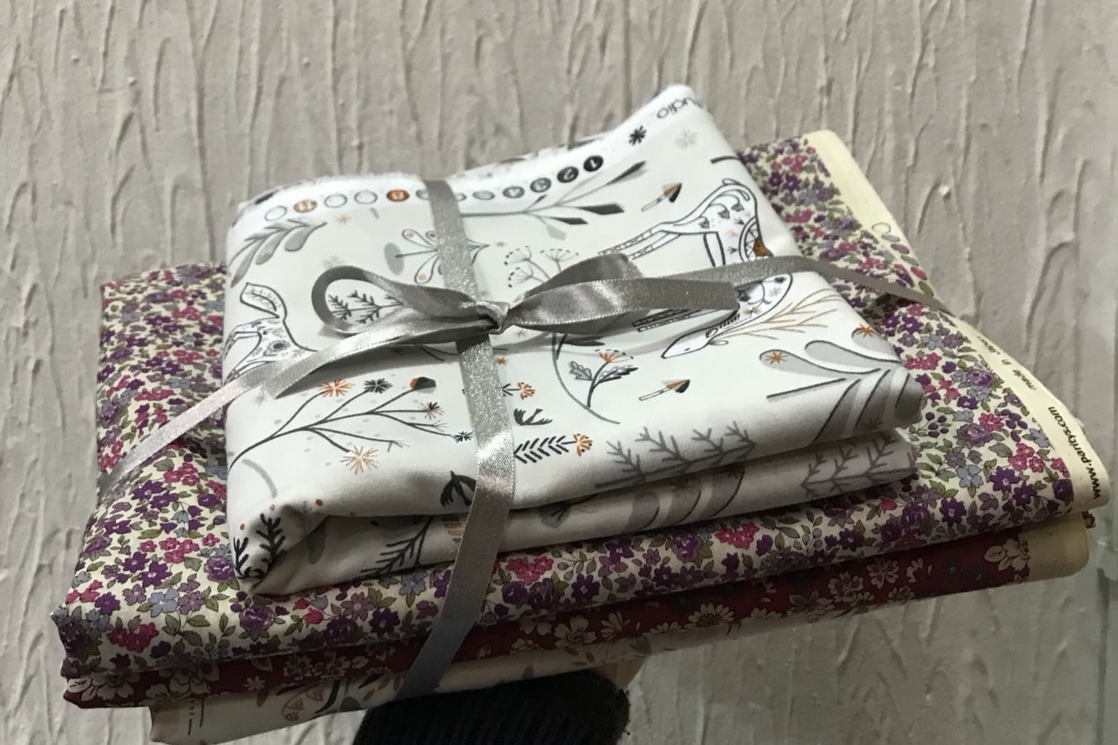 A customer's order: folded floral fabrics stacked and tied with a silver ribbon, held out on one hand.