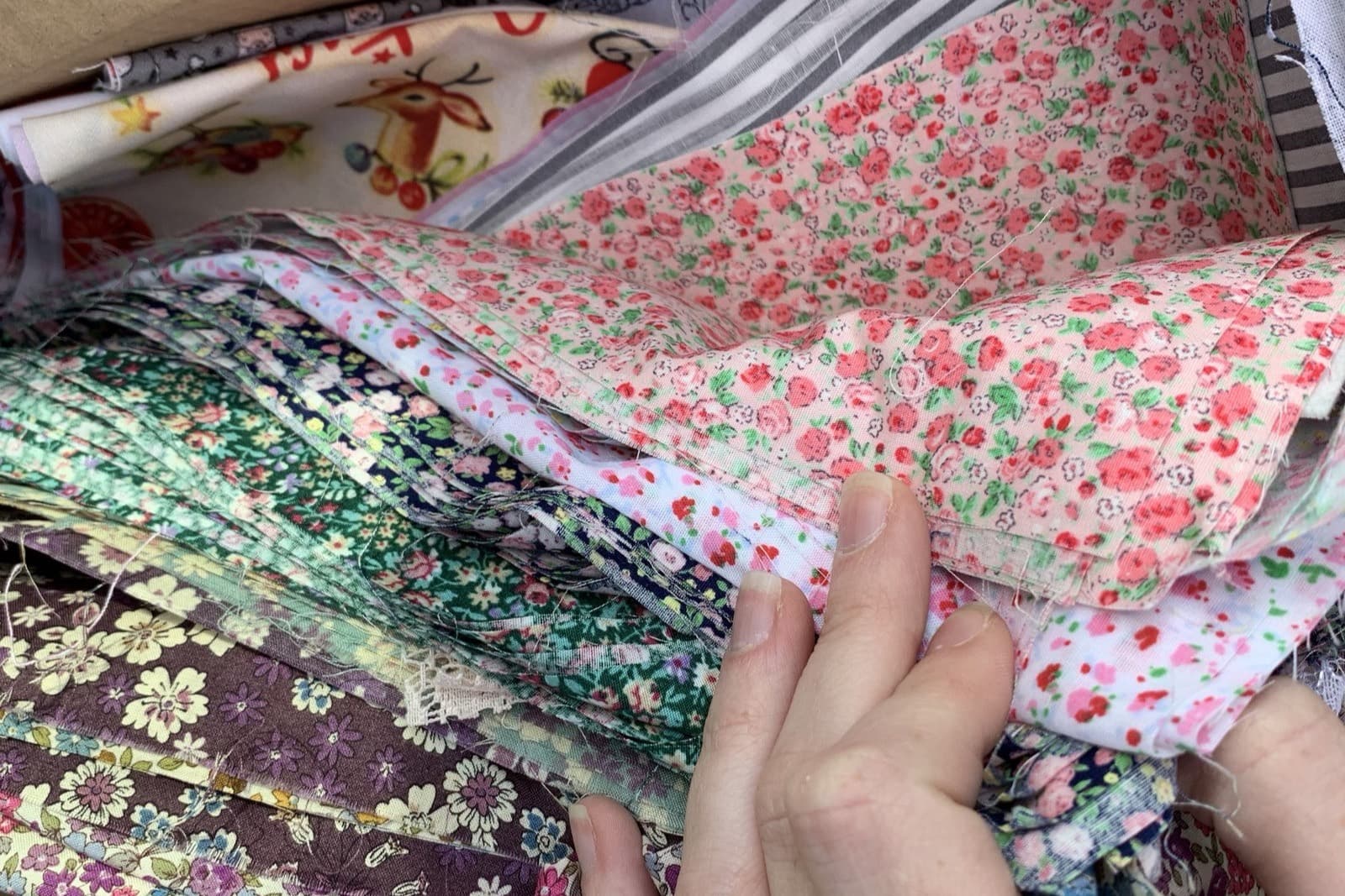 A cardboard box filled with floral cotton offcuts, a hand lifting a folded stack of them.