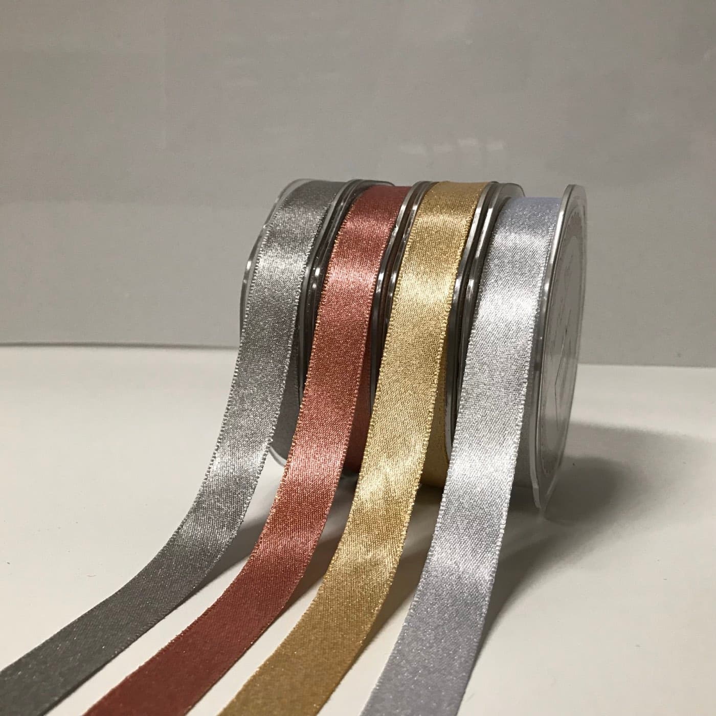 Spools of satin ribbon in silver, rose gold and gold, each unspooling in a steady run across the table.