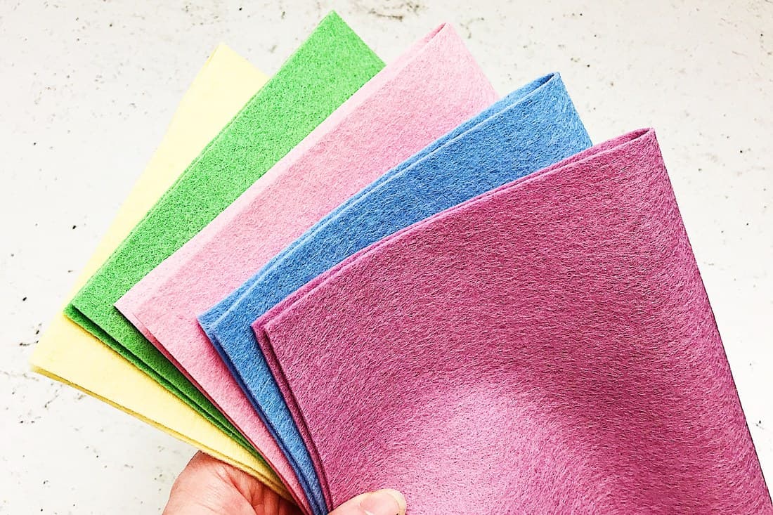 A hand fanning out sheets of felt in yellow, green, pink and blue