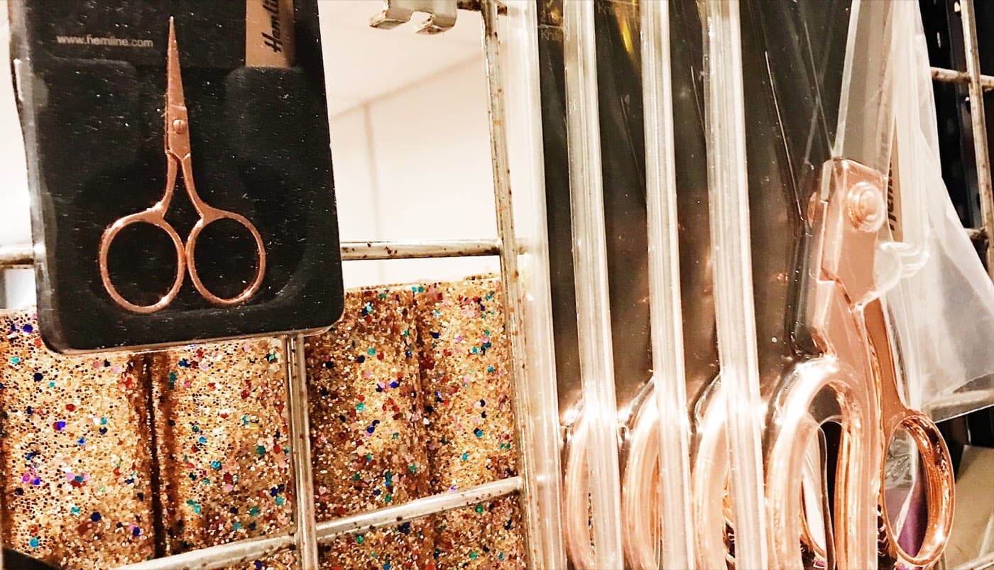 A retail display stand stocked with rose gold scissors and glitter fabric squares.