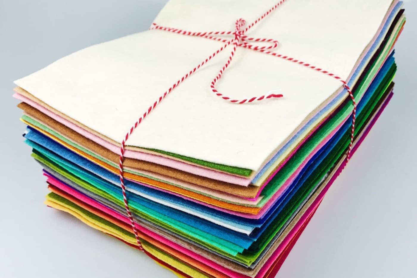 A stack of felt sheets in every colour, squared up and tied with red and white baker's twine.