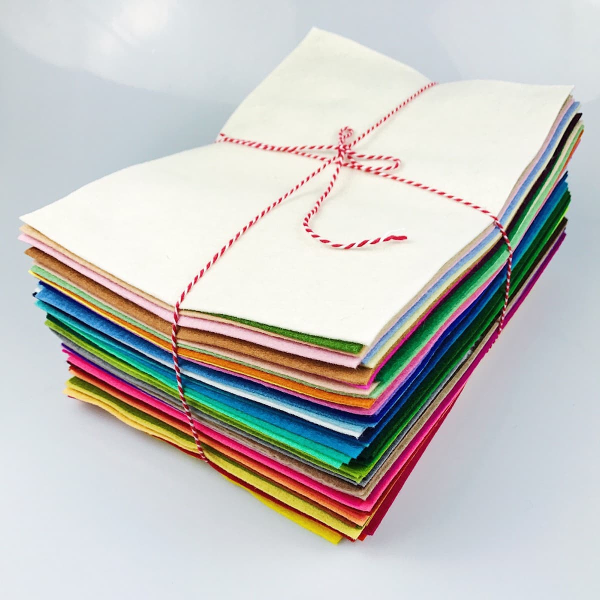 A stack of felt sheets in every colour, squared up and tied with red and white baker's twine.